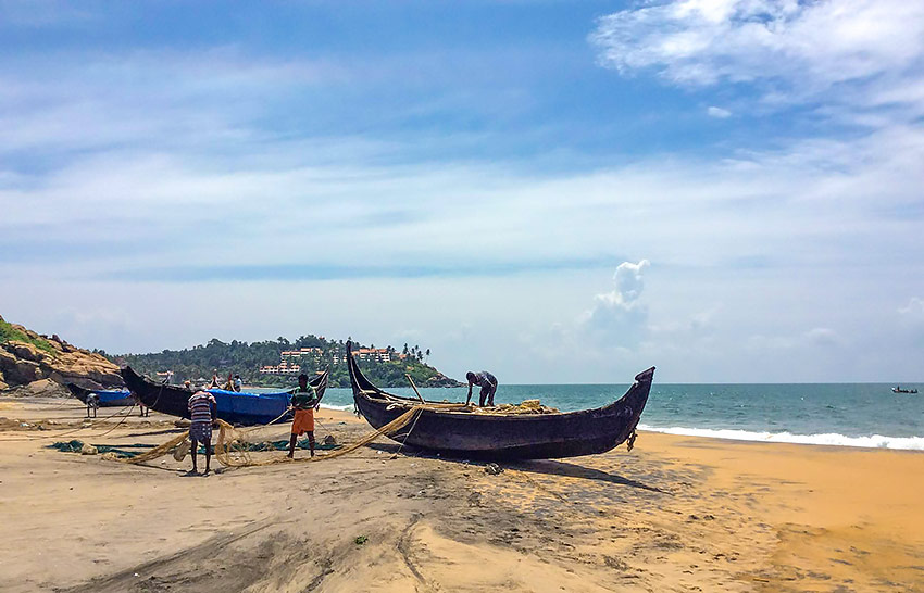 Lokala fiskemän med båtar på strand i Kerala